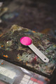 A measuring spoon resting on a weighing scale, used to precisely measure pigments for accurate colour mixing.